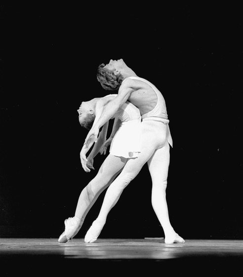 Heather Watts in a backbend, leaning onto Mikhail Baryshnikov, both in white simple costumes, in a performance of Apollo