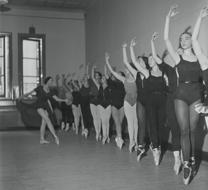 Dancers en pointe at the barre, one arm up
