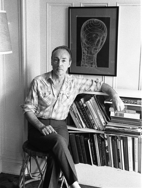 George Balanchine sitting cross-legged in front of a bookcase and line drawing