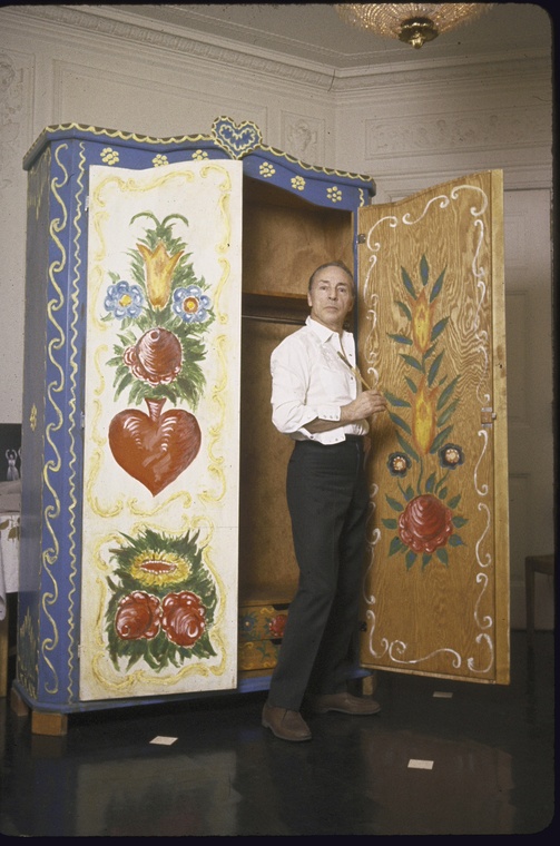 Balanchine standing paintbrush in hand in front of a cabinet he designed and painted