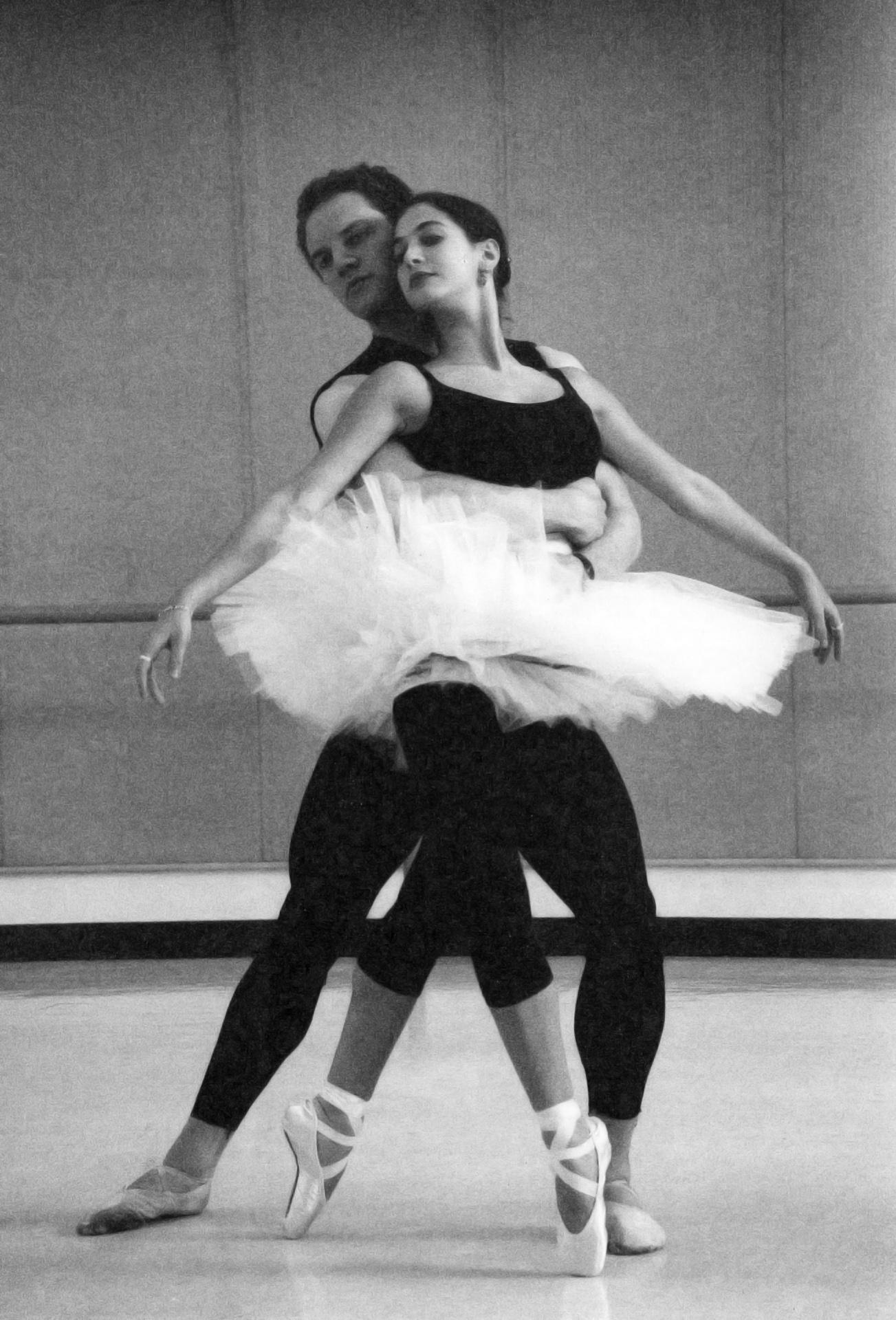 James Fayette, in all black, holding the waist of dancer Lilyan Vigo in a white tutu as she leans back onto him in a fourth position en pointe