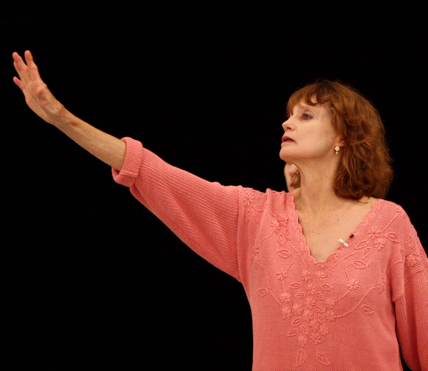 Suzanne Farrell in a decorative coral sweater looking towards her outstretched arm in a coaching session for Meditation